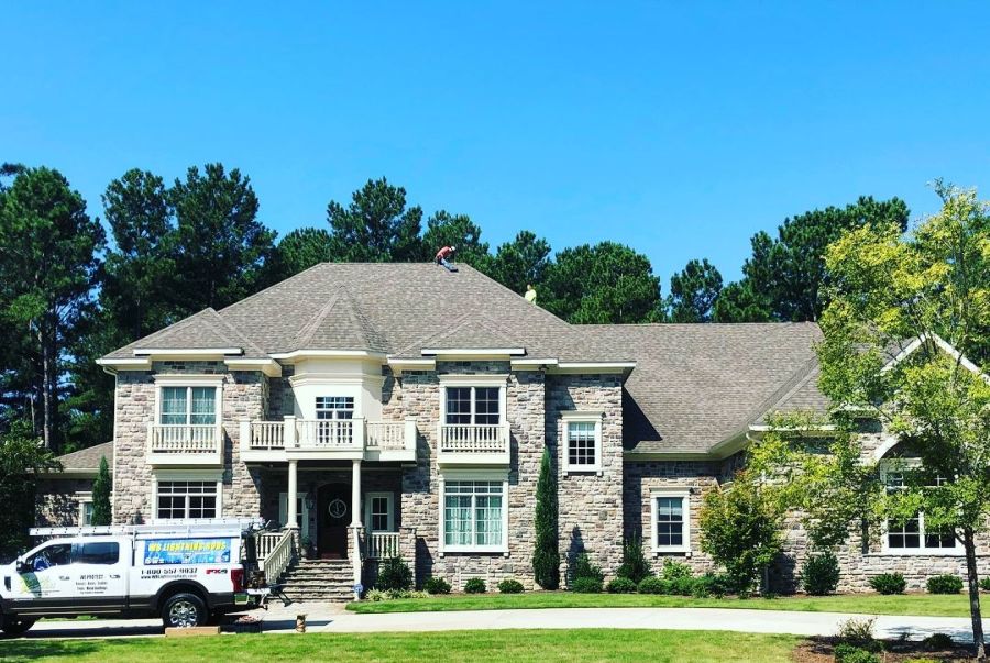 Technicians install lightning protection on a large stone house roof beside a service truck